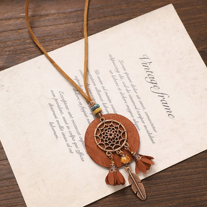 Dreamcatcher wooden necklace with brown circular pendant, feather and tassel charms on vintage paper background.