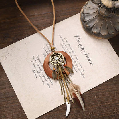Dreamcatcher-style tassel wooden necklace with bronze web pendant, feathers, and beads on vintage paper.
