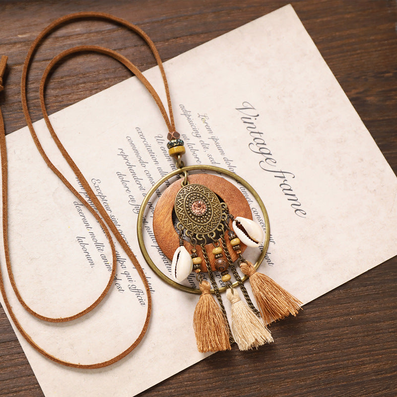 Ethnic oval pendant tassel wooden necklace with shells, beads, and beige tassels on brown table background.