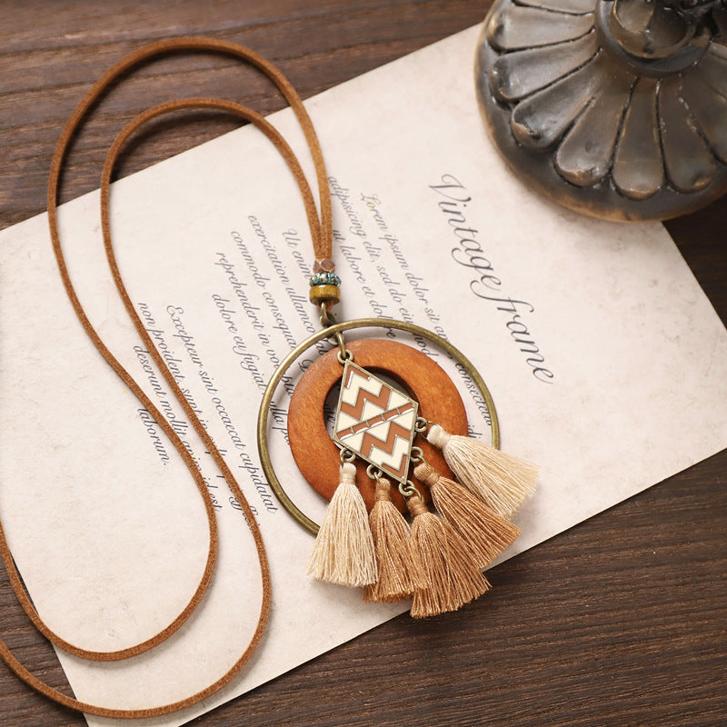 Tassel wooden necklace with geometric pendant and layered beige fringe displayed on rustic background.