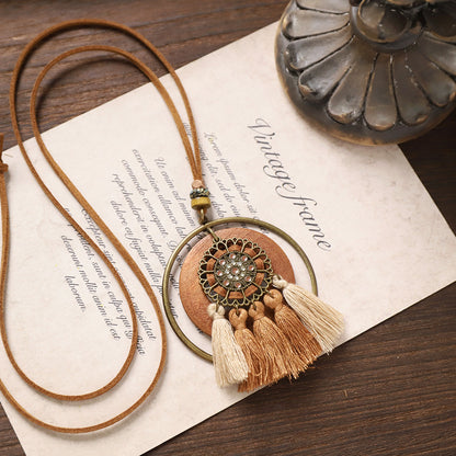 Layered circular wooden necklace with ornate metallic centerpiece and triple beige tassels.