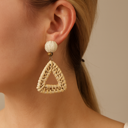 Close-up of triangular hand-woven rattan earring with cream fiber bead worn by woman.