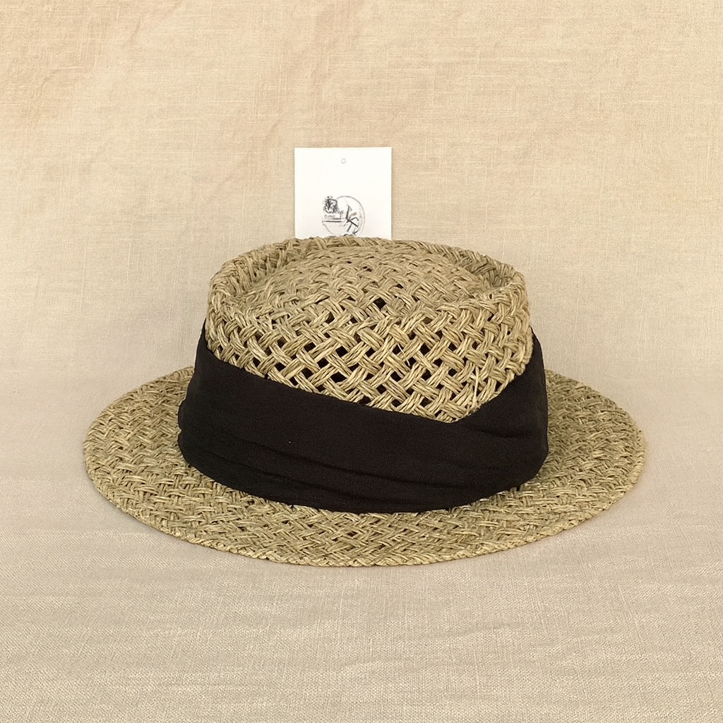Handcrafted vintage straw hat with black ribbon accent, displayed on a neutral linen background.