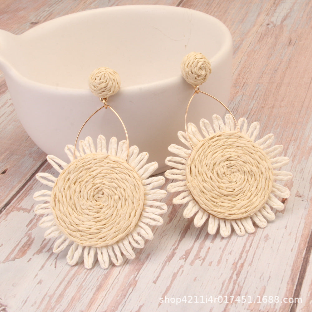 White woven sunflower earrings with natural raffia texture and gold wire loop design.