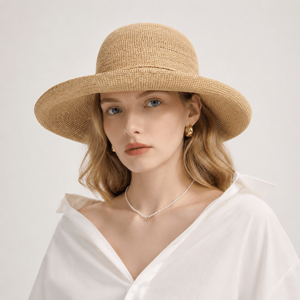 Woman wearing a beige woven wide brim straw sun hat with bow detail and white blouse