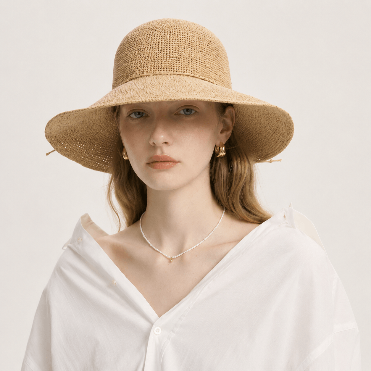 Woman styled in a white blouse wearing a woven wide brim straw hat for summer