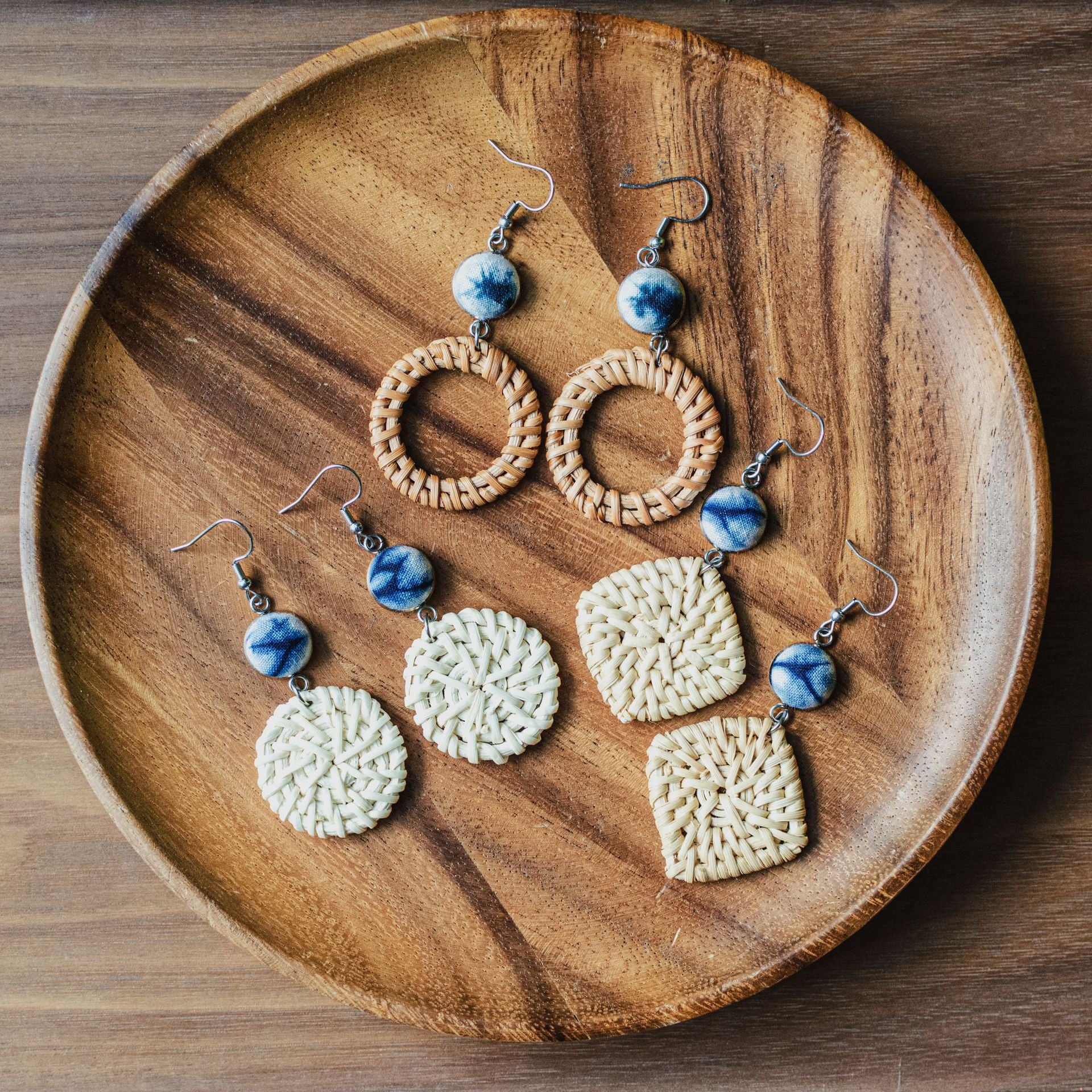 Set of natural vine and straw earrings with blue ceramic beads displayed on wooden plate.