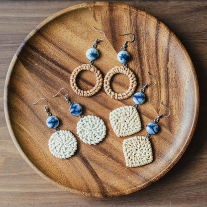 Set of natural vine and straw earrings with blue ceramic beads displayed on wooden plate.