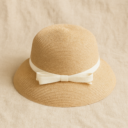 Natural straw hat with white ribbon bow, placed on linen fabric background highlighting handwoven texture.