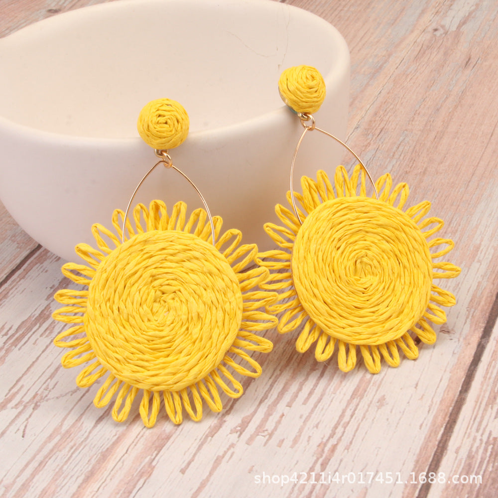 Yellow sunflower-shaped woven earrings crafted from Lafite grass on rustic wood background.